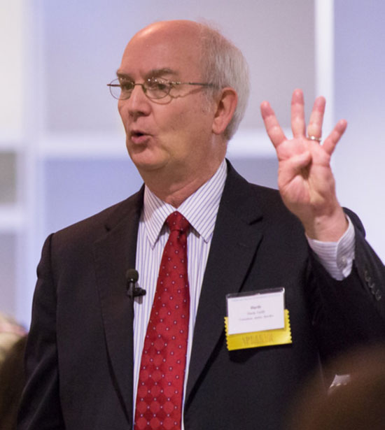 Hardy Smith in a suit, speaking and holding up four fingers.